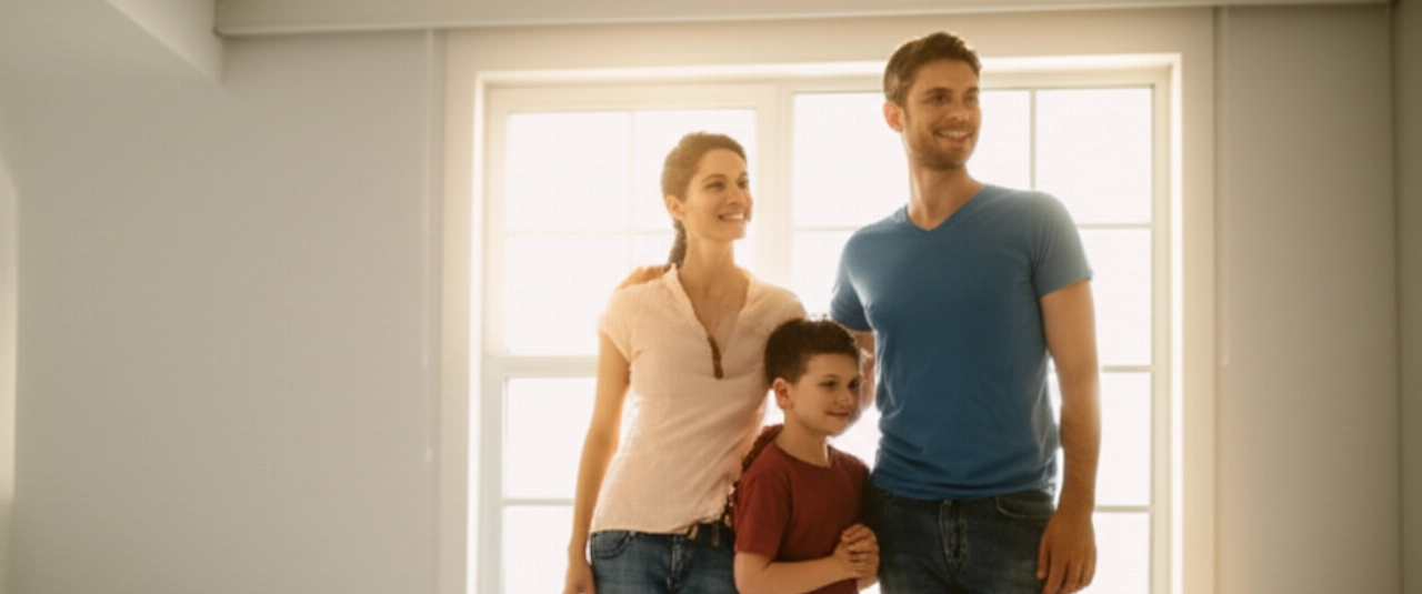 Une famille caucasienne heureuse sourit dans une pièce lumineuse de leur nouvelle maison, symbolisant un déménagement réussi et un nouveau départ.